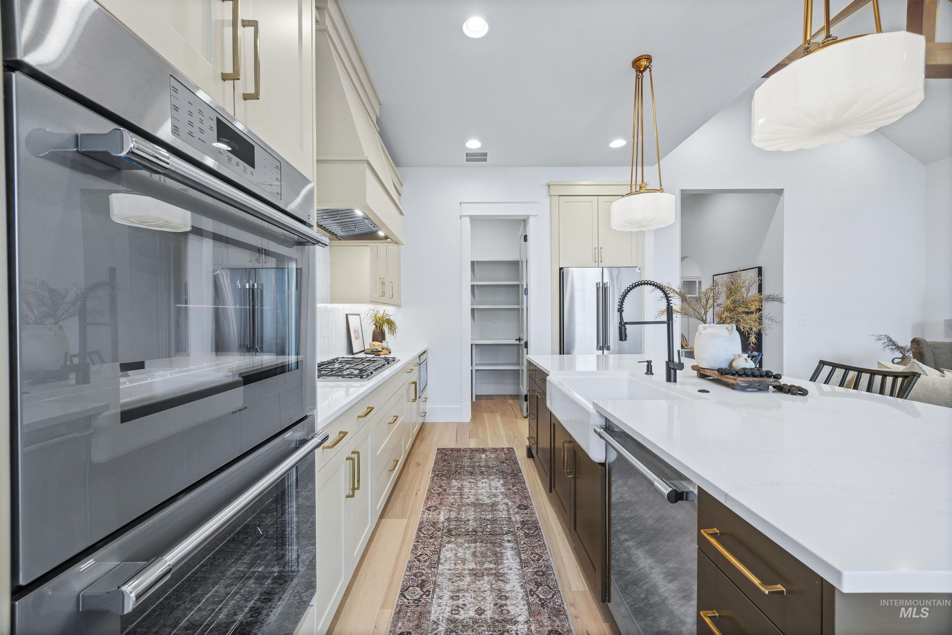 948 East Escalation Street Meridian, ID 83642 - Photo 20 of 44 Kitchen featuring two tone cabinetry, stainless steel appliances, light stone countertops, decorative light fixtures, and light wood-type flooring