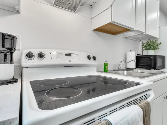 a utility room with a sink a stove and white cabinets