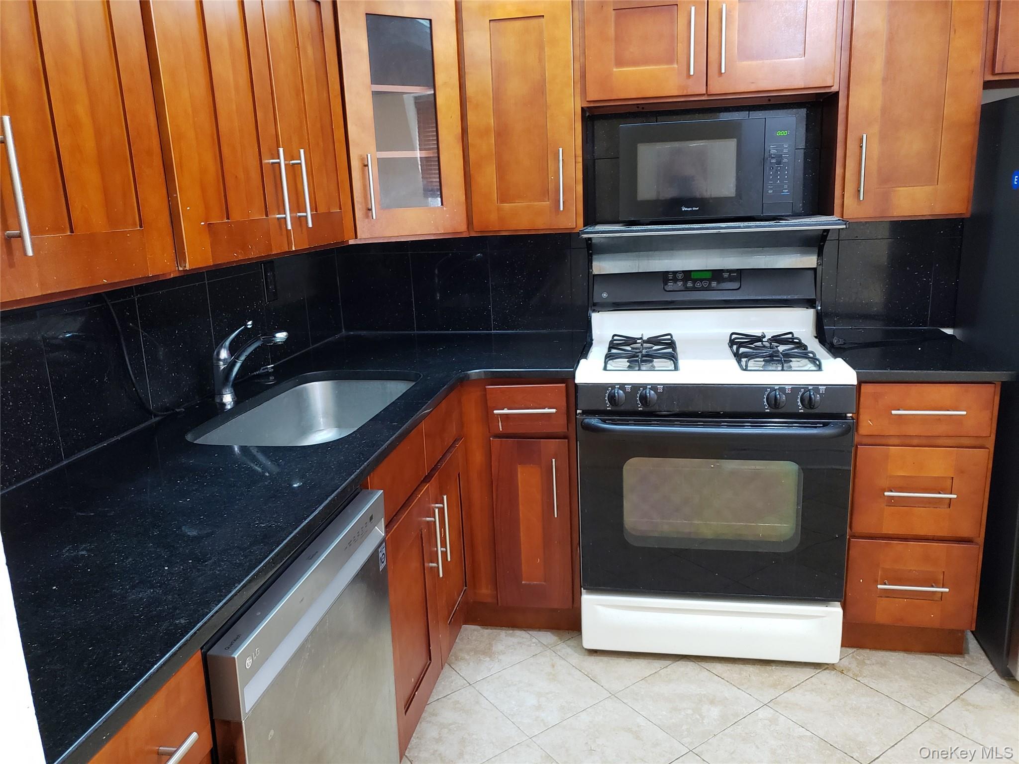 12-30 Estates Lane, Unit 2 Queens, NY 11360 - Photo 5 of 9 Kitchen with black appliances, brown cabinetry, dark stone countertops, and light tile patterned floors