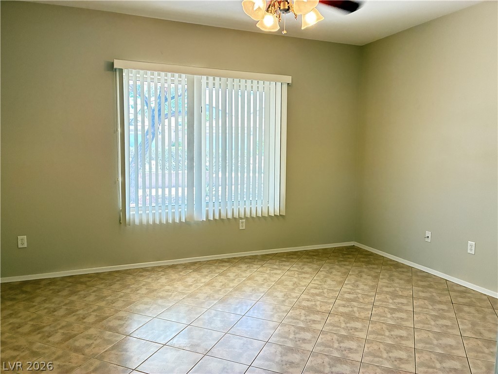 A versatile space features tiled flooring, a wide window with vertical blinds, and a ceiling fan for comfort.