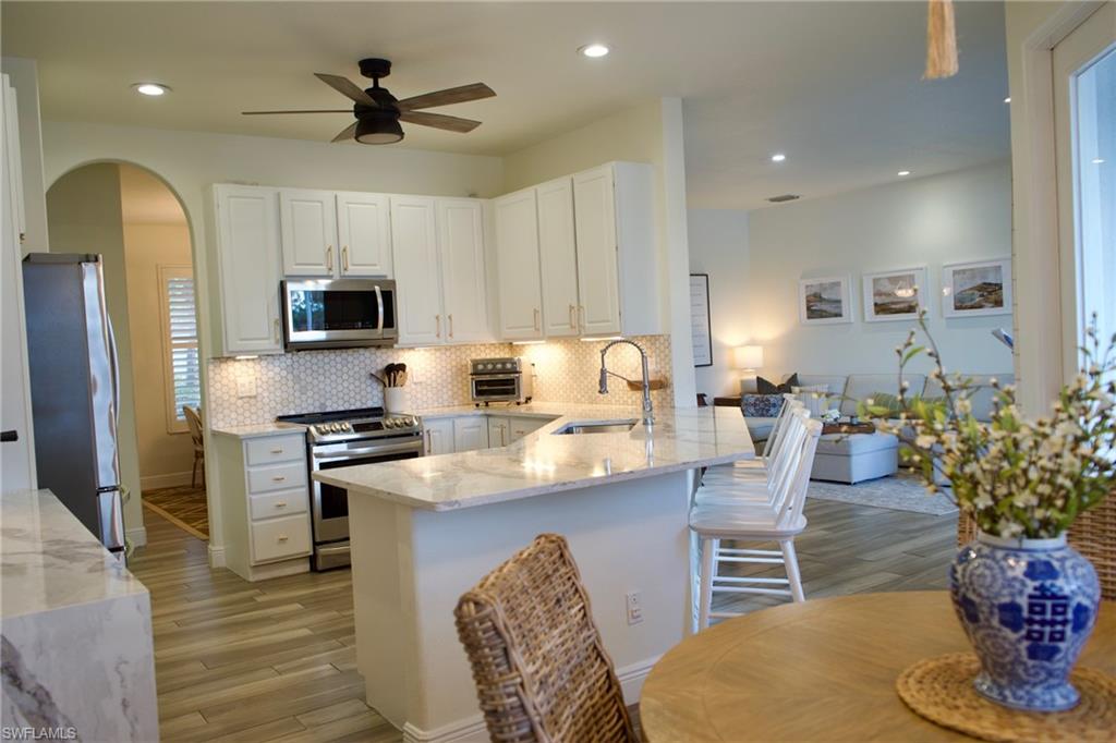 3944 Ruxton Road Naples, FL 34116 - Photo 7 of 27 a kitchen with stainless steel appliances granite countertop a stove refrigerator a sink dishwasher a dining table and chairs with wooden floor