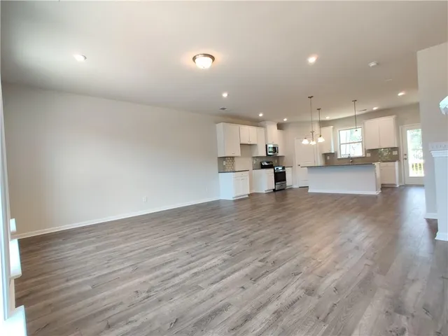a view of an empty room and kitchen with wooden floor