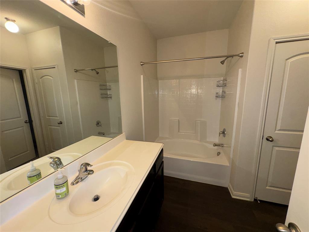 14360 Riata Lane Dallas, TX 75253 - Photo 7 of 16 Bathroom featuring a dark wood-finish vanity, a white countertop with an integrated sink, a large wall-mounted mirror, and a white tub/shower combination with a chrome fixture