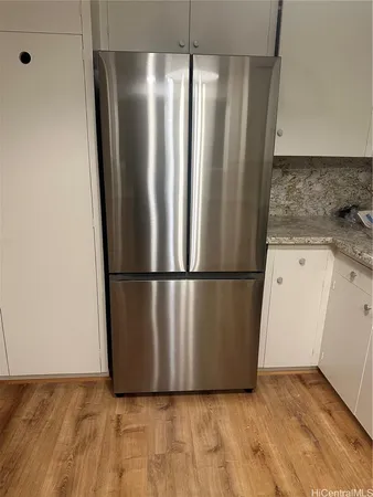 a view of a refrigerator in kitchen and an empty room with wooden floor
