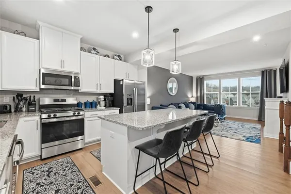 a kitchen with stainless steel appliances granite countertop a stove a refrigerator a kitchen island a dining table and chairs with wooden floor