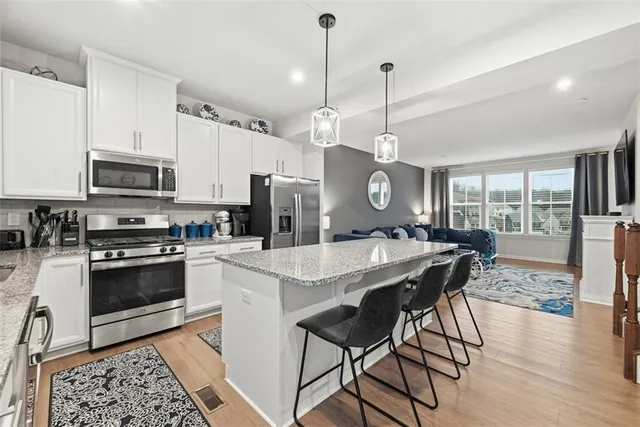 a kitchen with stainless steel appliances granite countertop a stove a refrigerator a kitchen island a dining table and chairs with wooden floor