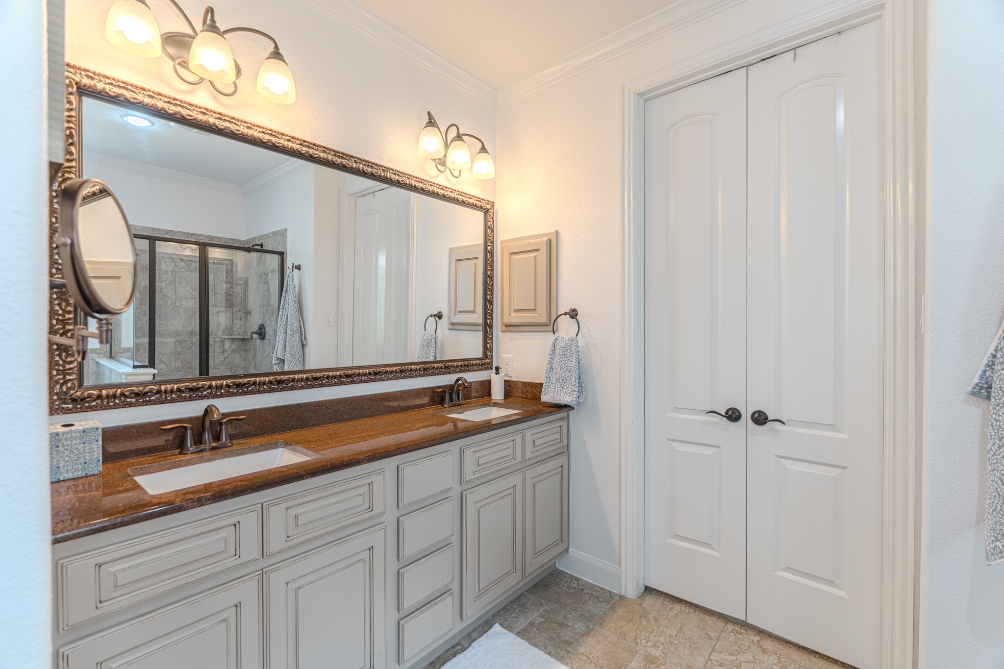 30 Fury Ranch Place The Woodlands, TX 77375 - Photo 28 of 47 This bathroom features a spacious layout with a dual-sink vanity, elegant lighting, a large framed mirror, and ample cabinet storage. It includes a glass-enclosed shower and a separate bathtub, complemented by neutral tile flooring and wall accents for a modern, clean look.