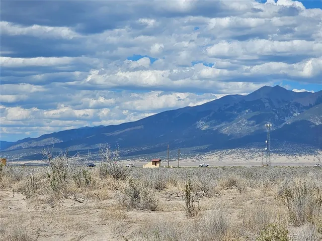 a view of a dry yard with mountains and a large tree