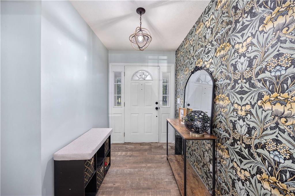 62 McCarthy Road Opelika, AL 36804 - Photo 18 of 74 Entryway featuring a decorative accent wall with botanical print wallpaper, wood-finish flooring, a white paneled entry door with sidelights, and an overhead pendant light fixture
