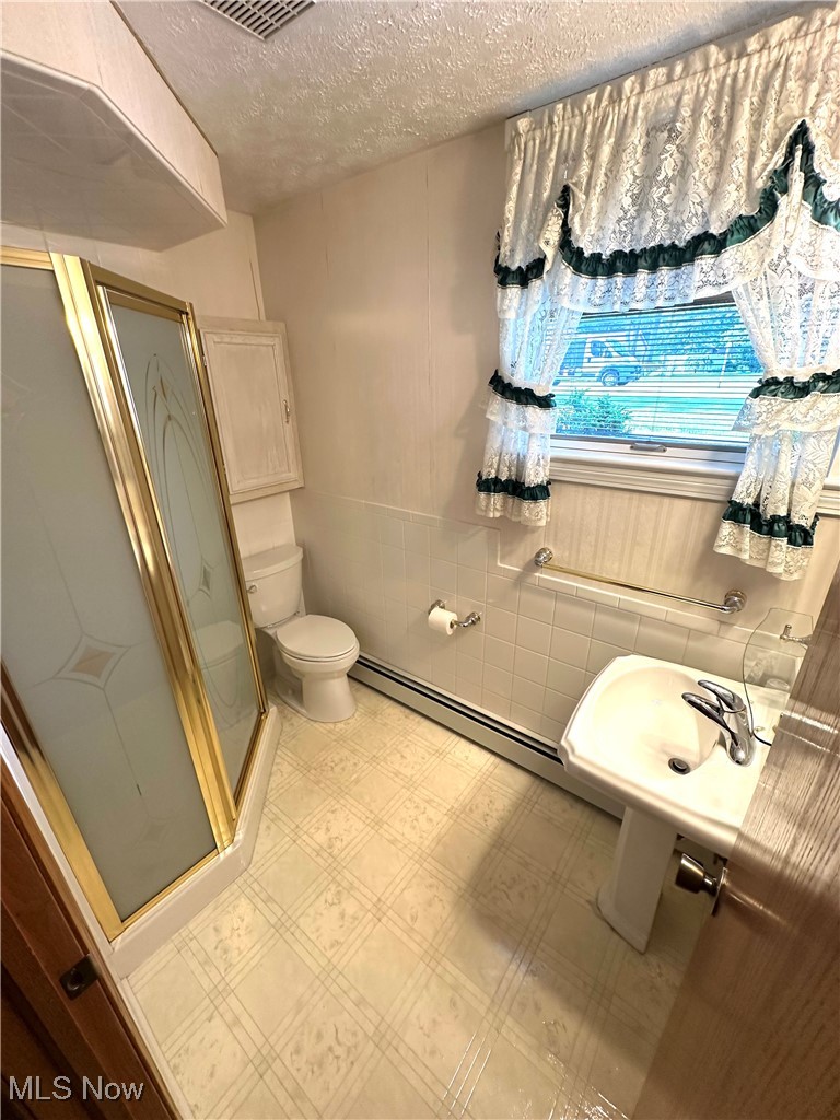 1684 Morris Street Mineral Ridge, OH 44440 - Photo 44 of 50 Full bath with a shower stall, toilet, a textured ceiling, a baseboard heating unit, and tile patterned floors