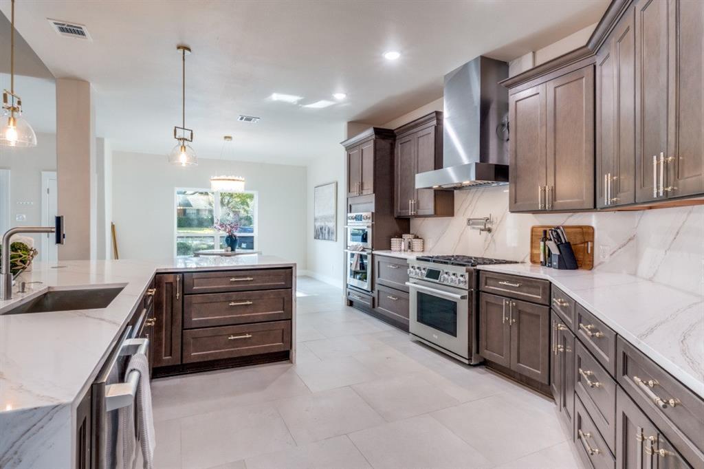 7115 Meadow Road Dallas, TX 75230 - Photo 7 of 22 Gourmet kitchen featuring a large island, stainless steel appliances, dark wood cabinetry, a pot filler, and white countertops