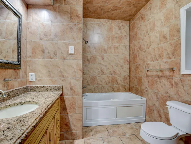 a bathroom with a granite countertop bathtub sink vanity mirror and toilet