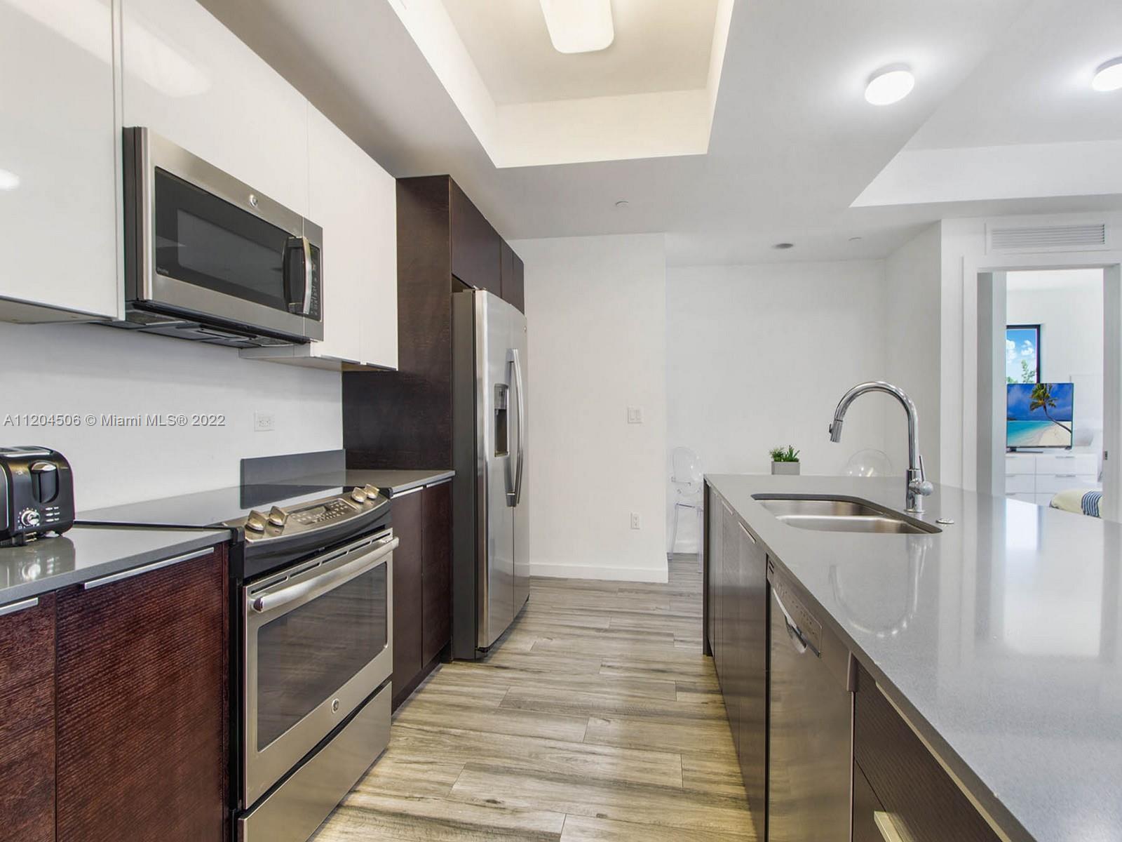 2955 Bird Avenue, Unit PHA Miami, FL 33133 - Photo 4 of 33 a kitchen with stainless steel appliances granite countertop a sink and a stove top oven with wooden floor
