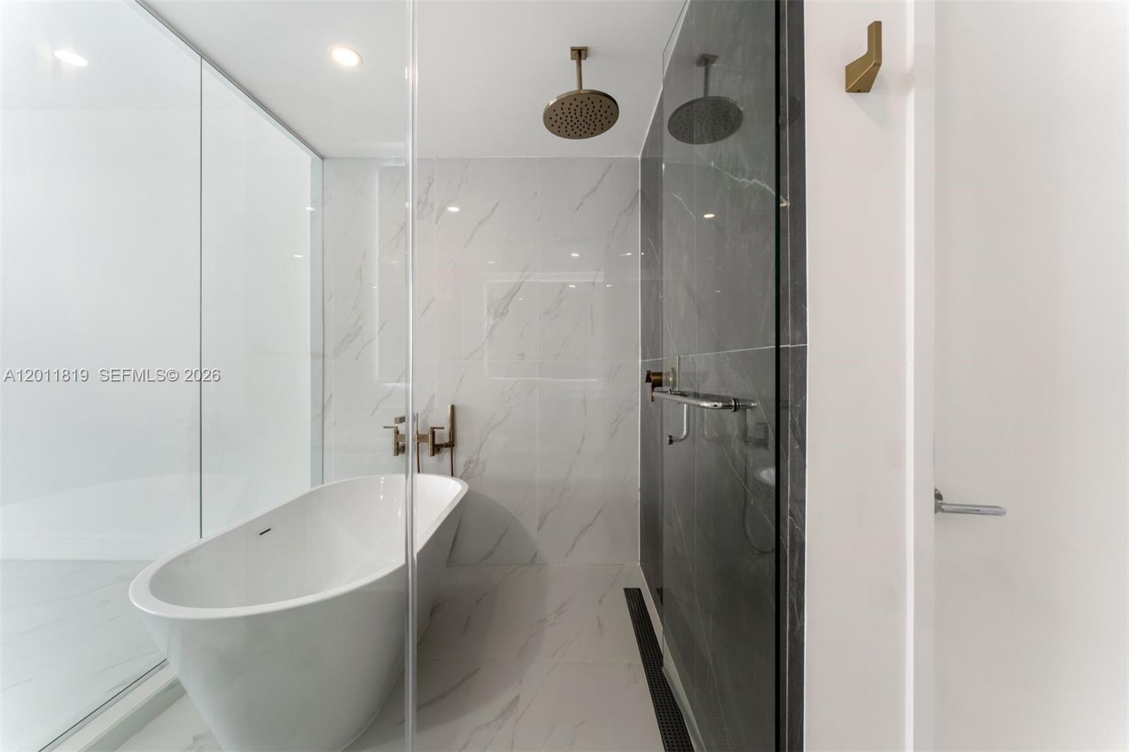700 Northeast 24th Street, Unit 2504 Miami, FL 33137 - Photo 5 of 52 Spa-inspired primary bathroom featuring dual vanities, a deep soaking tub, a frameless glass rainfall shower, and designer porcelain tile throughout.