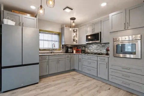 a kitchen with stainless steel appliances granite countertop a refrigerator a sink dishwasher a stove and white cabinets with wooden floor