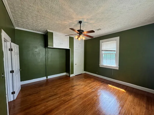 an empty room with wooden floor fan and windows