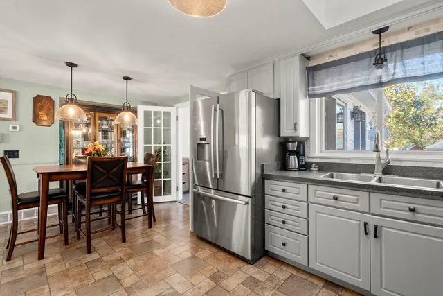 a kitchen with stainless steel appliances granite countertop a refrigerator a sink dishwasher a dining table and chairs with wooden floor