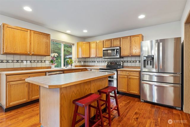 a dining hall with stainless steel appliances granite countertop a stove top oven a sink dishwasher and chairs with wooden floor