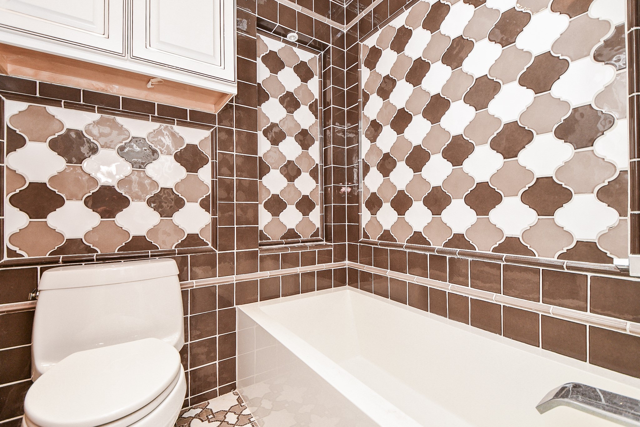 263 Wood Loop Street Houston, TX 77015 - Photo 42 of 45 This bathroom features a modern design with stylish brown and white patterned tiles, a clean white bathtub, and ample cabinet storage above the toilet.