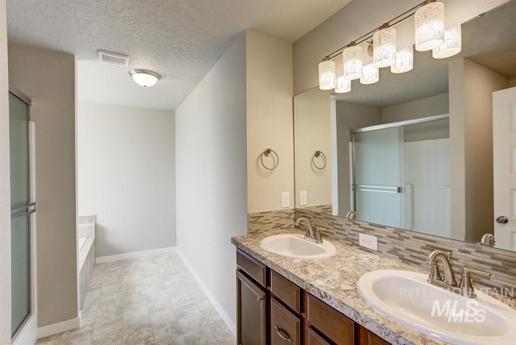 1589 Witt Mountain Mountain Home, ID 83647 - Photo 2 of 7 Bathroom with a shower stall, double vanity, a bath, backsplash, and a textured ceiling