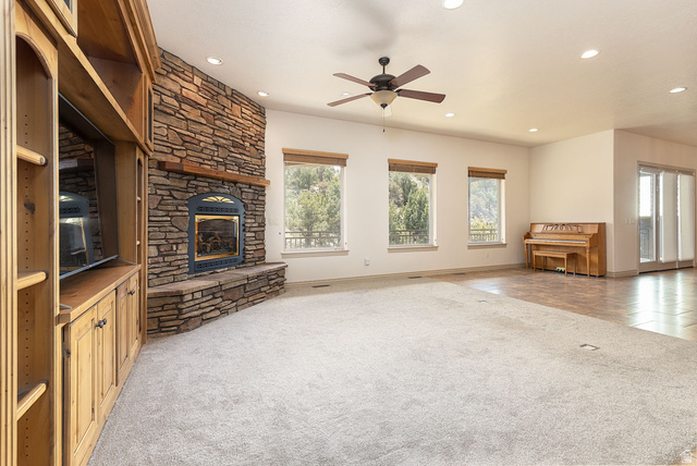 888 East Fiddlers Canyon Road Cedar City, UT 84721 - Photo 12 of 74 Unfurnished living room with light carpet, a stone fireplace, ceiling fan, and recessed lighting