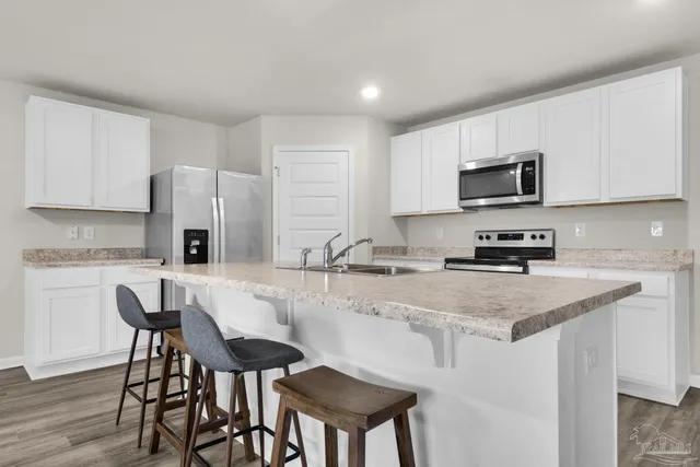 a kitchen with stainless steel appliances granite countertop a stove a sink a microwave a refrigerator and white cabinets with wooden floor