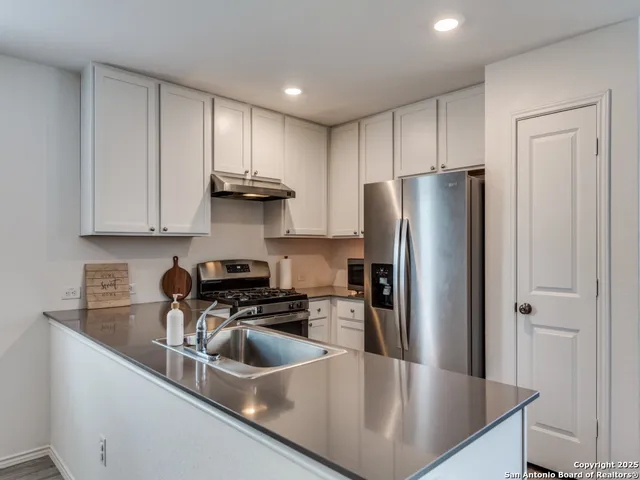 a kitchen with stainless steel appliances granite countertop a refrigerator a stove a sink and white cabinets