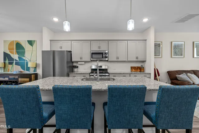 a kitchen with stainless steel appliances granite countertop a stove a sink a microwave a dining table and chairs with wooden floor