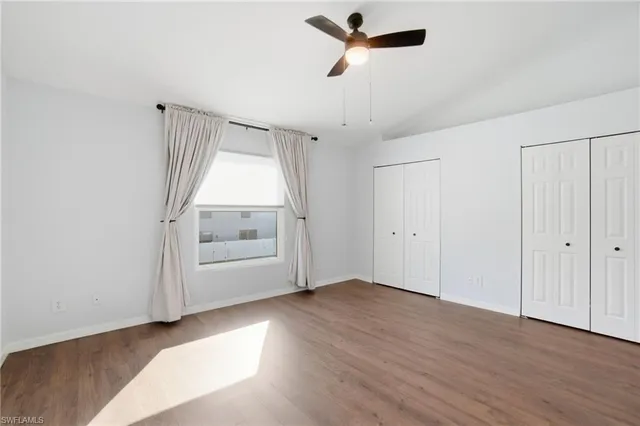 an empty room with wooden floor chandelier fan and windows