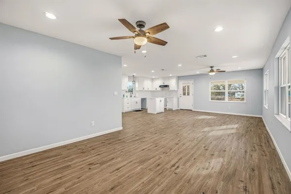 an empty room with wooden floor a ceiling fan and windows