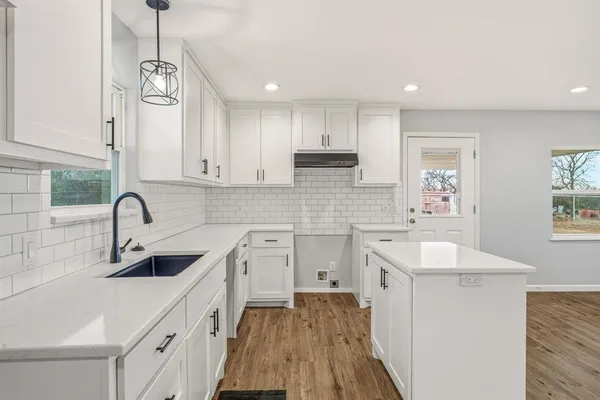 a kitchen with a sink dishwasher a stove and white cabinets with wooden floor