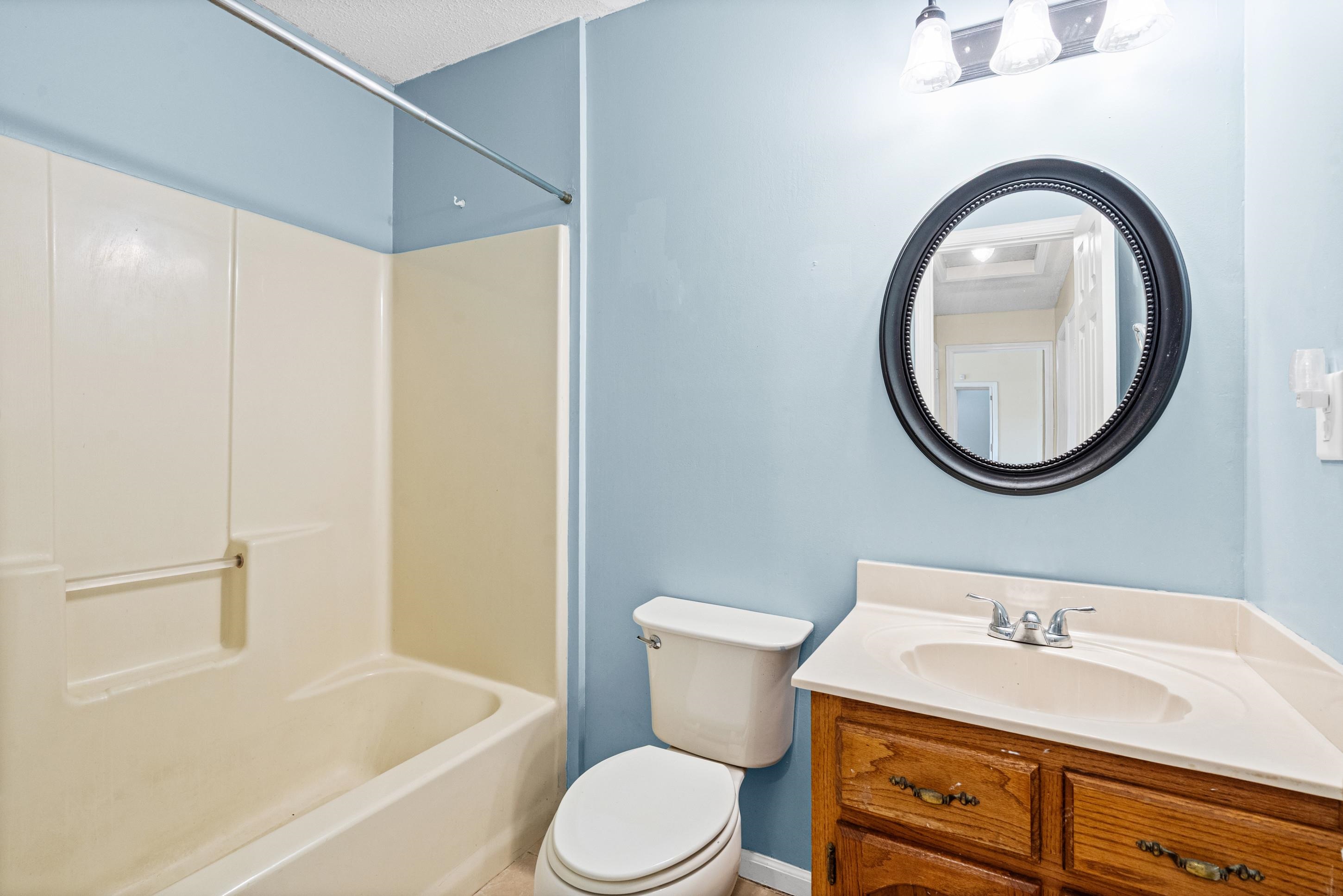 7130 Bryan Station Road Cordova, TN 38018 - Photo 17 of 26 Bathroom featuring a combination bathtub and shower unit, a wood-finish vanity with an integrated sink, a dark framed round mirror, and a three-light vanity fixture