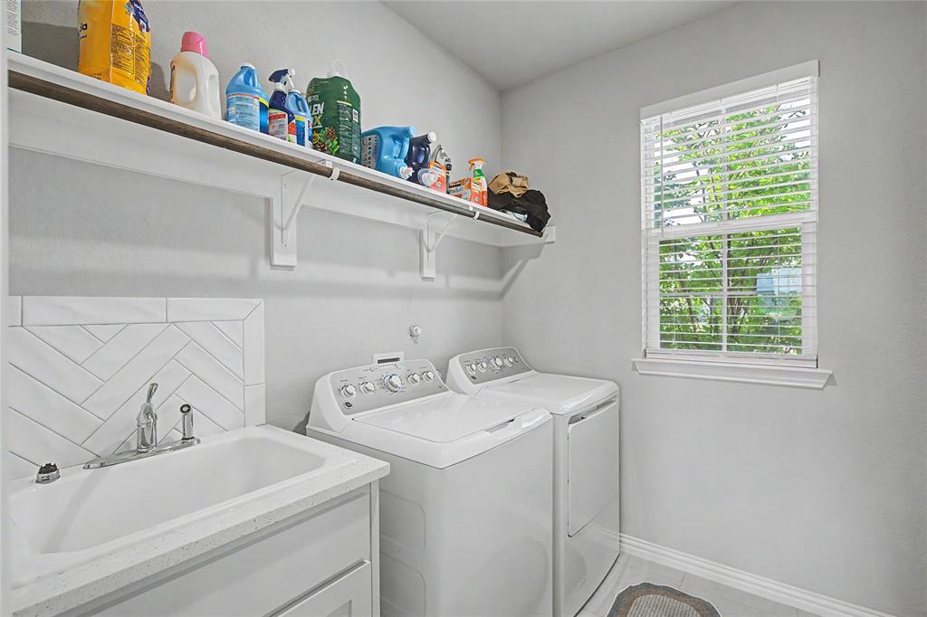 185 Chester Road Springtown, TX 76082 - Photo 33 of 40 Laundry room featuring a utility sink with a stone-finish countertop, herringbone tile backsplash, open shelving, and a window for natural light