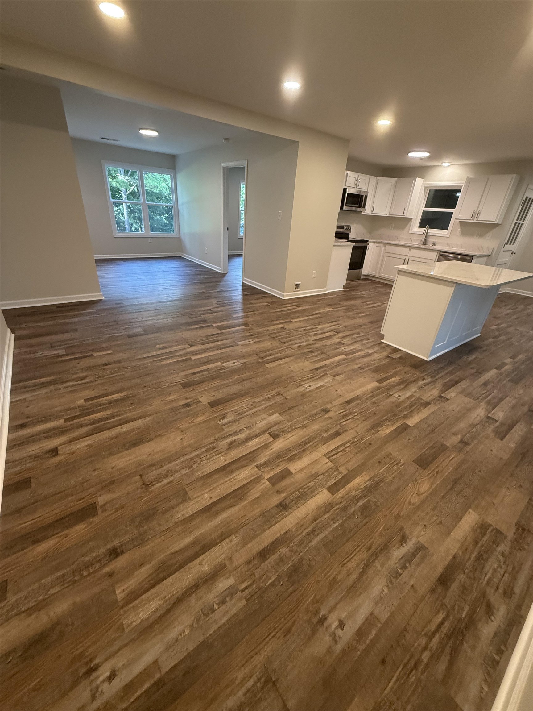 Open-concept  featuring wood-finish flooring, recessed lighting, and a kitchen with white cabinetry, stainless steel appliances, and a central island with countertop seating