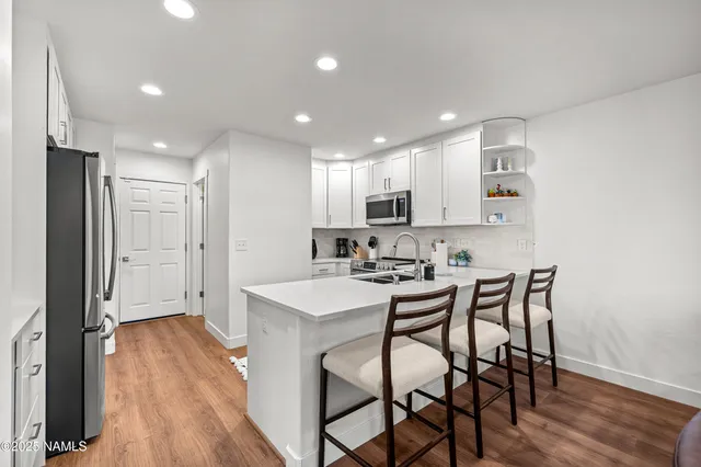 a kitchen with stainless steel appliances a sink a stove a refrigerator with wooden floor and cabinets