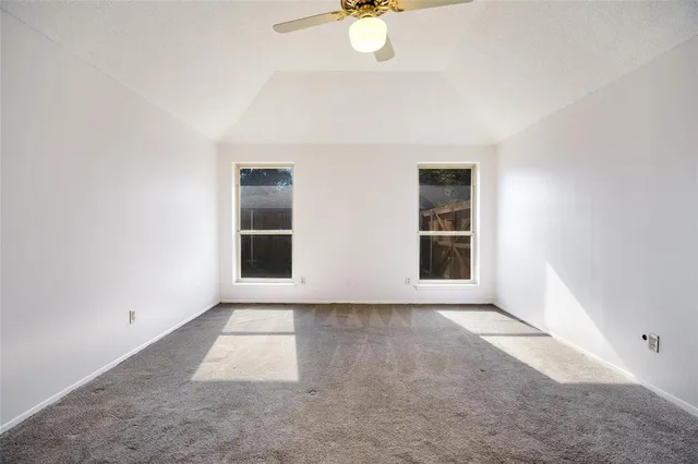 an empty room with chandelier fan and windows