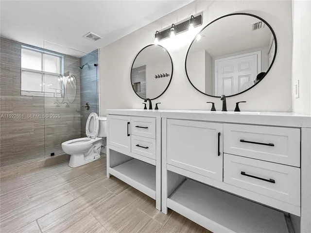 a bathroom with a toilet a double vanity sink and a mirror