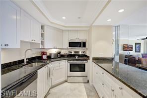 1 Bluebill Avenue, Unit 707 Naples, FL 34108 - Photo 10 of 16 Kitchen with ceiling fan, sink, stainless steel appliances, dark stone countertops, and white cabinets