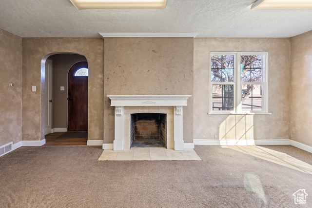 465 North Main Street Richfield, UT 84701 - Photo 13 of 43 Unfurnished living room featuring a tiled fireplace, a textured ceiling, carpet floors, arched walkways, and baseboards