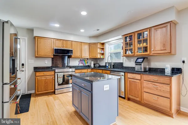 a kitchen with stainless steel appliances granite countertop a stove top oven a sink dishwasher a refrigerator and white cabinets with wooden floor