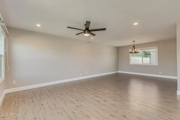 an empty room with wooden floor ceiling fan and windows