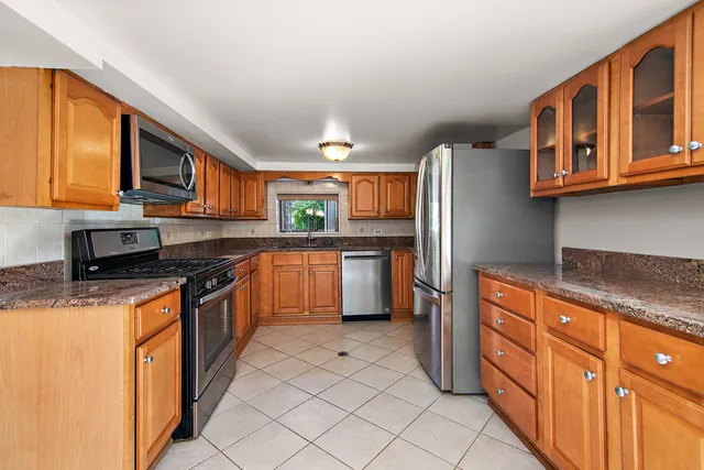 a kitchen with stainless steel appliances granite countertop a stove top oven a sink dishwasher and a refrigerator with wooden cabinets