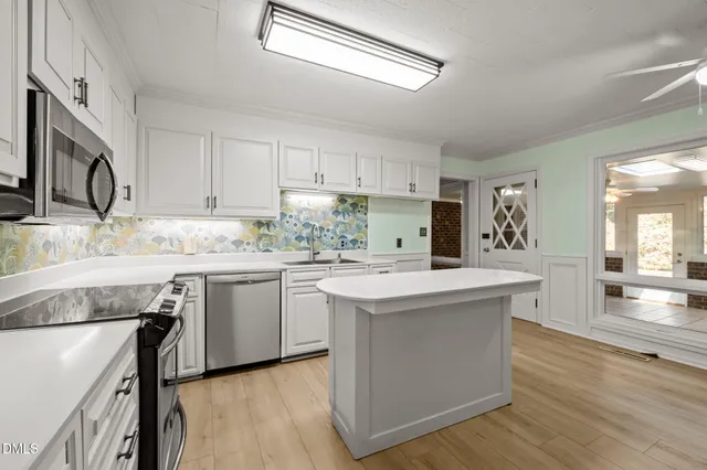 a kitchen with stainless steel appliances granite countertop a refrigerator a stove a sink and white cabinets with wooden floor