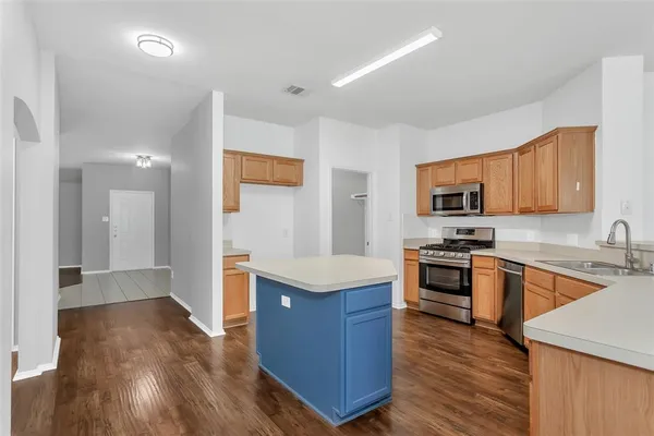 a kitchen with stainless steel appliances granite countertop a stove top oven a sink dishwasher and a refrigerator with wooden floor