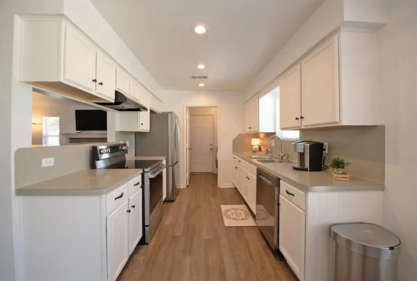 a kitchen with stainless steel appliances granite countertop a stove top oven a sink dishwasher and a refrigerator with wooden floor