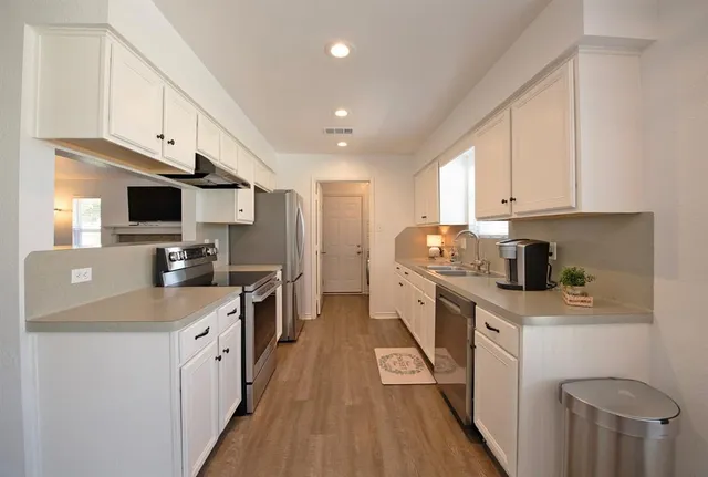 a kitchen with stainless steel appliances granite countertop a stove top oven a sink dishwasher and a refrigerator with wooden floor