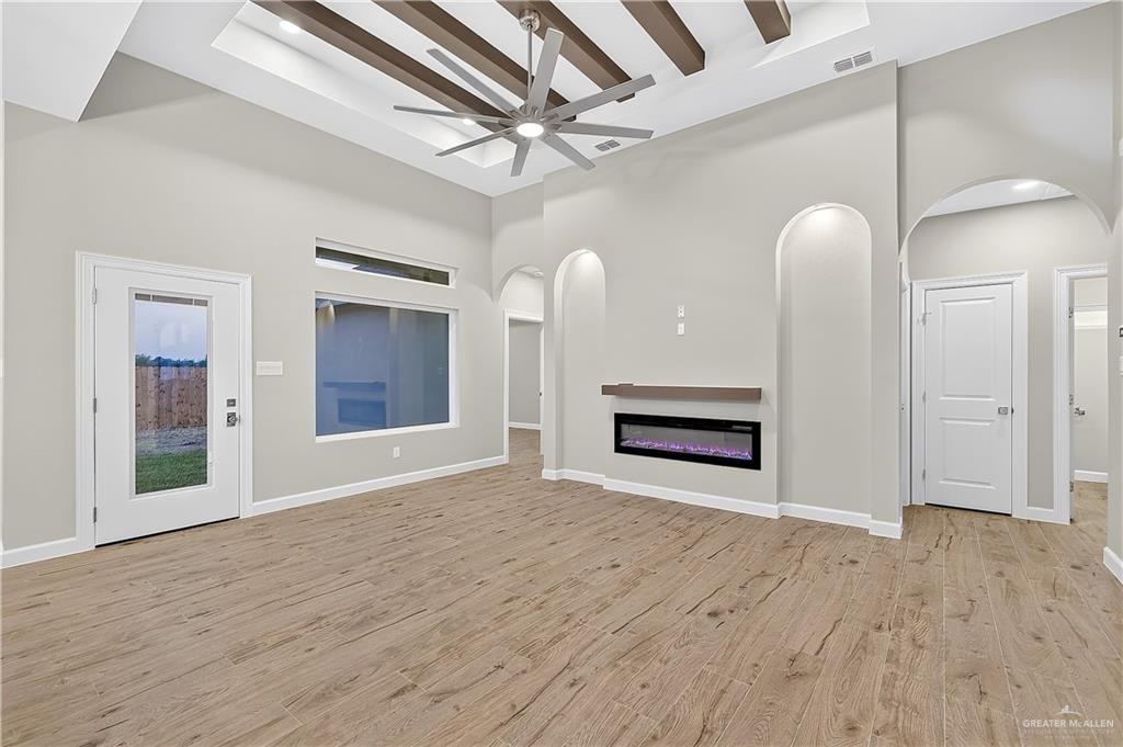 431 Sandy Road Donna, TX 78537 - Photo 10 of 28 Vaulted ceiling with exposed wood-finish beams, wood-finish flooring, electric fireplace with floating mantel, arched wall niches with accent lighting, and a glass-paneled exterior door