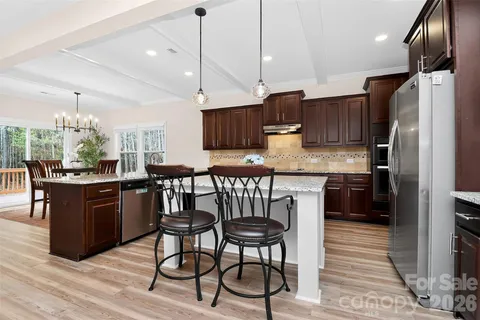 a kitchen with stainless steel appliances granite countertop a refrigerator a stove a sink a dining table and chairs with wooden floor