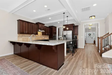 a kitchen with stainless steel appliances granite countertop a refrigerator a sink dishwasher a stove and a dining table with wooden floor