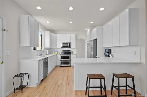 a kitchen with stainless steel appliances kitchen island granite countertop a stove a sink a refrigerator and white cabinets with wooden floor